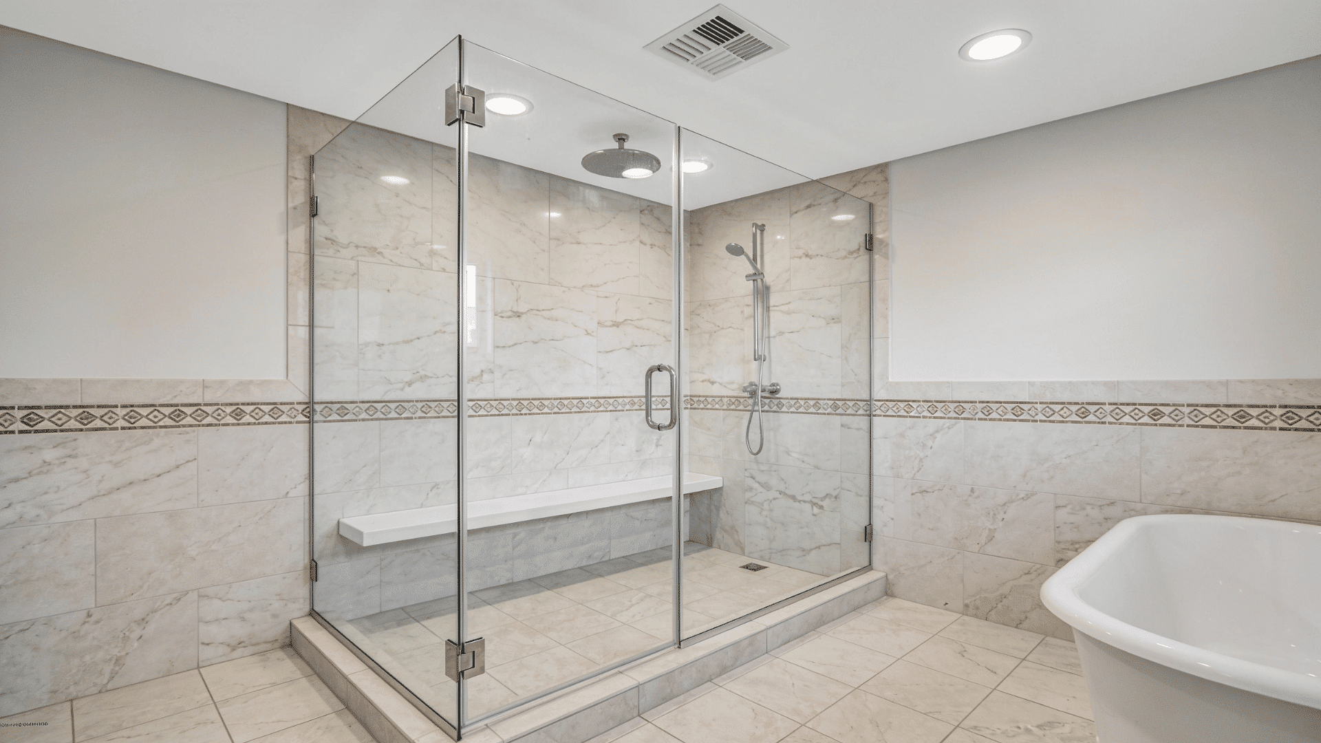 frameless glass shower with marble-look tiles, built-in bench, and chrome fixtures