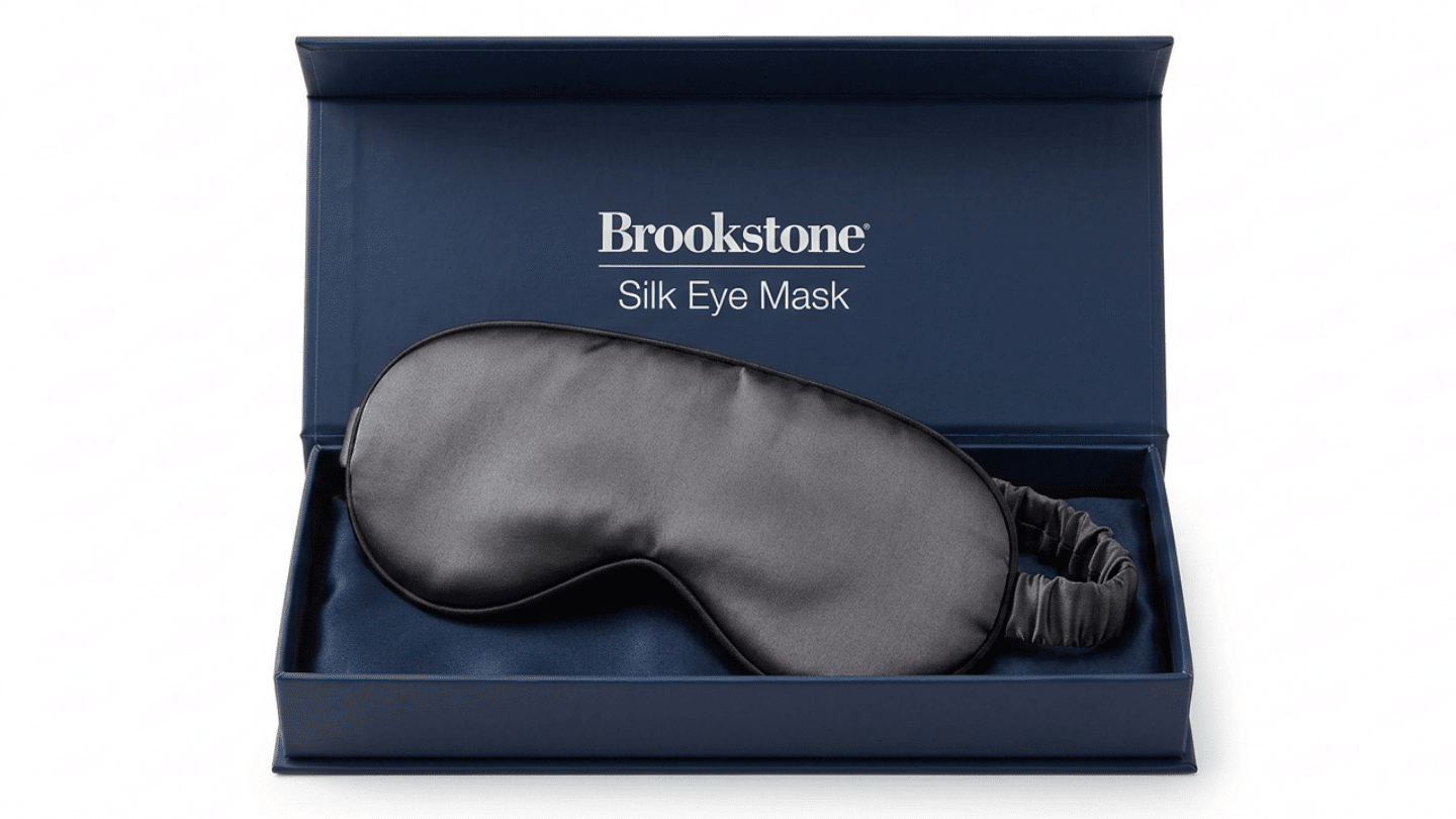 gray Brooklinen silk sleep mask displayed inside an open navy presentation box on white studio scene