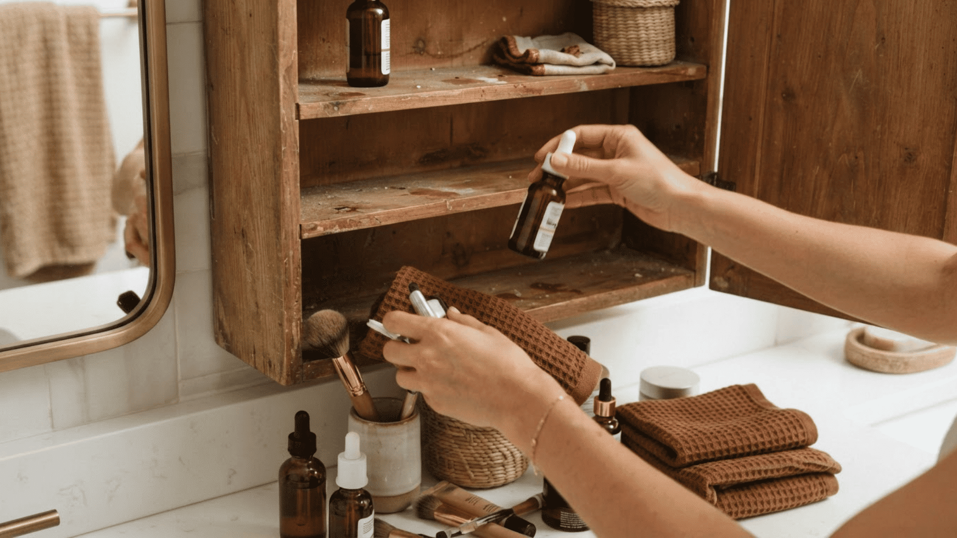 hands removing toiletries from an open wooden bathroom cabinet before organizing shelves