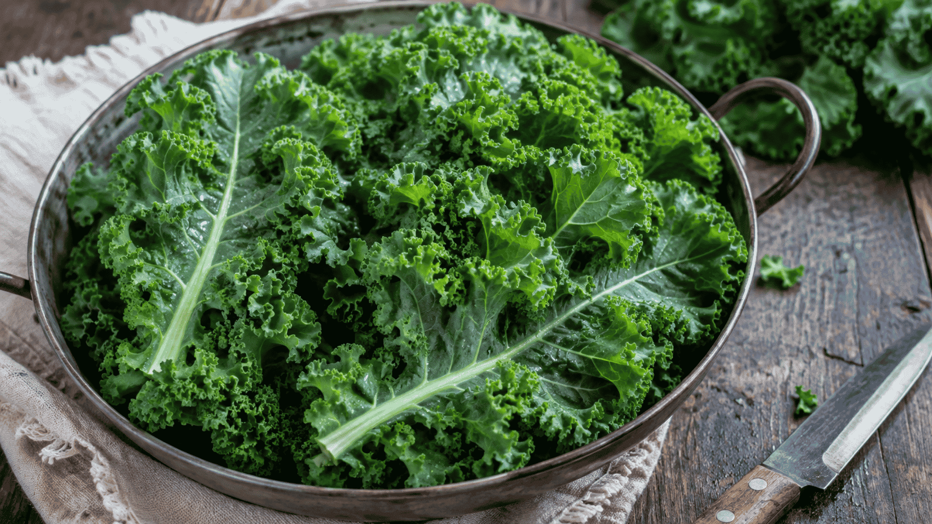 fresh curly kale leaves arranged in a metal bowl on a rustic wooden table