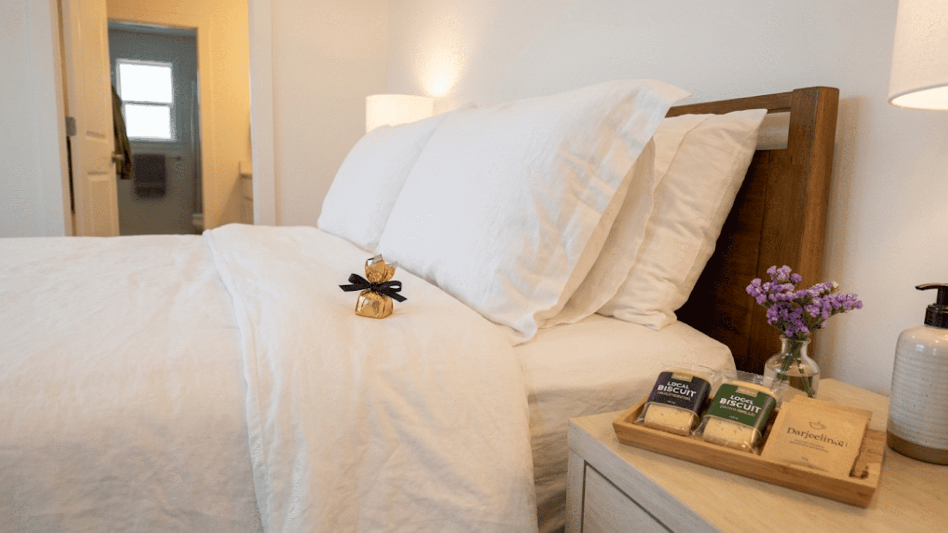 Gold-wrapped chocolate on a white guest bed next to a tea and biscuit tray.