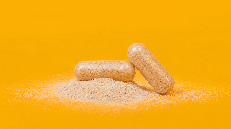 close-up of two psyllium fiber capsules resting on a small pile of beige powder against a bright yellow background