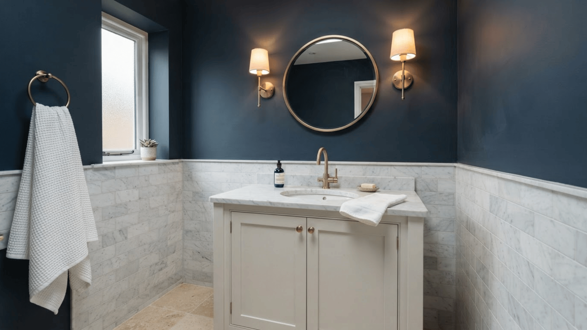 navy blue bathroom with white vanity, marble wall tile, brass fixtures, and round mirror