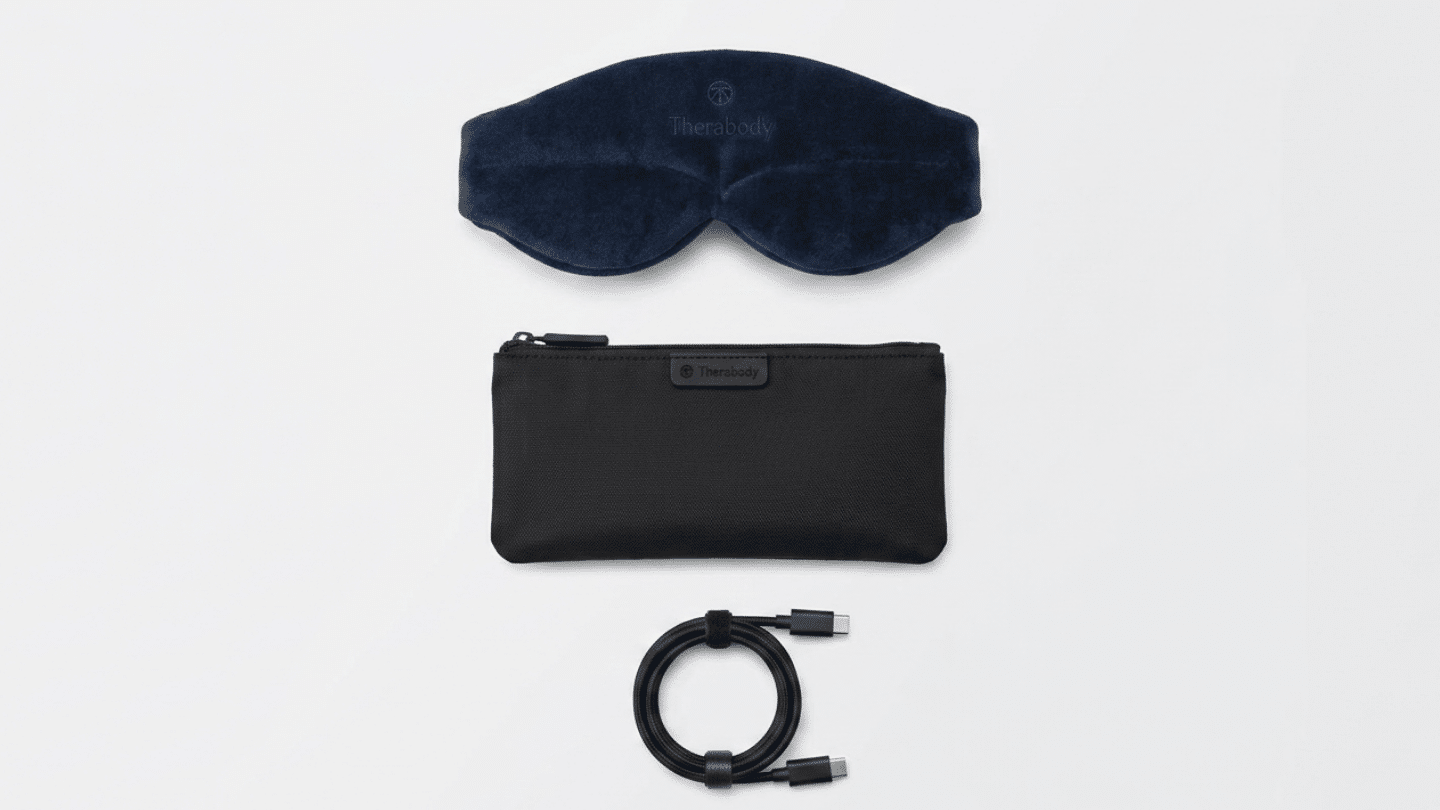 navy Therabody sleep mask with black storage pouch and coiled charging cable placed on white surface