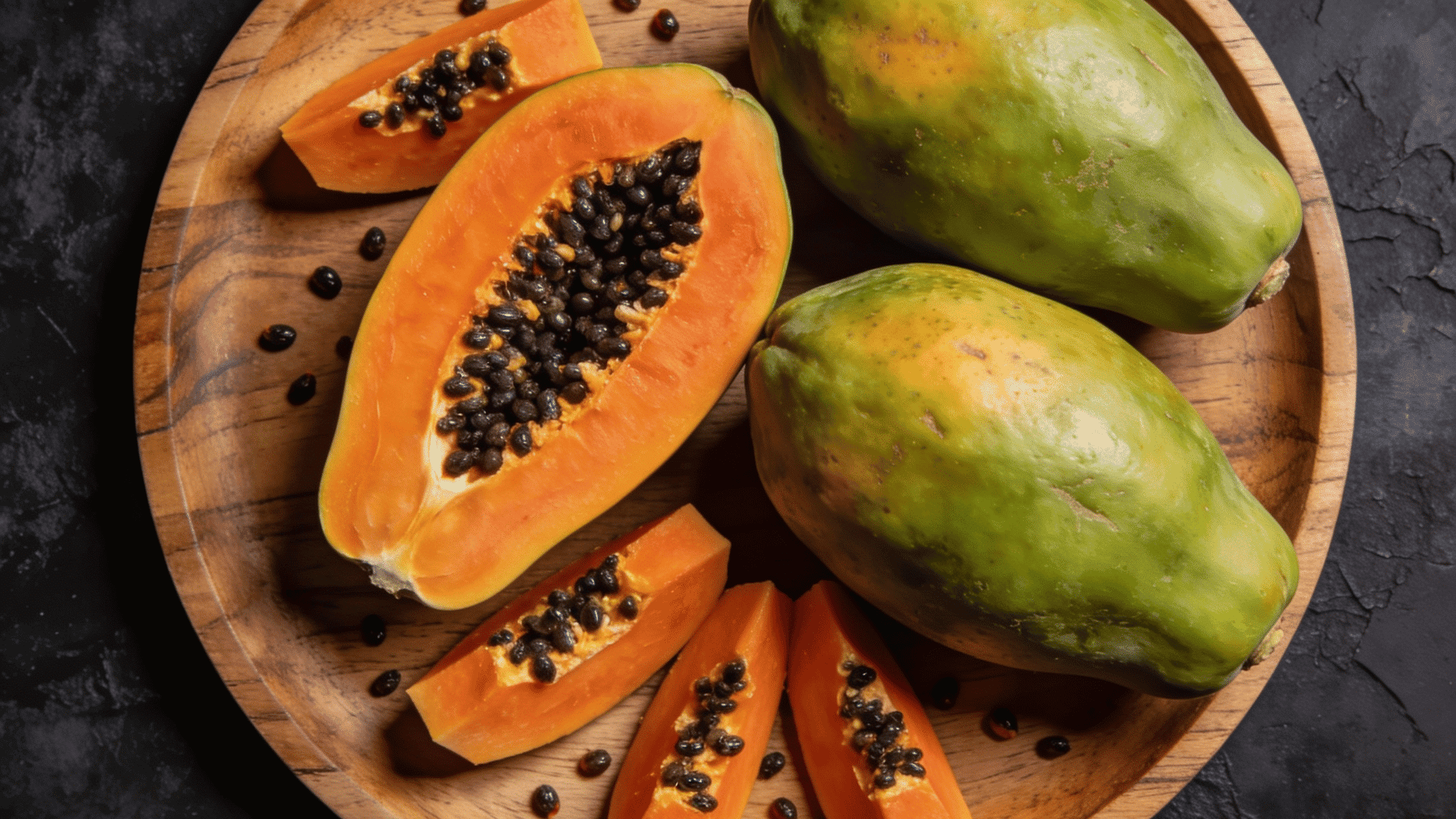 whole and sliced papayas with orange flesh and black seeds on a wooden tray