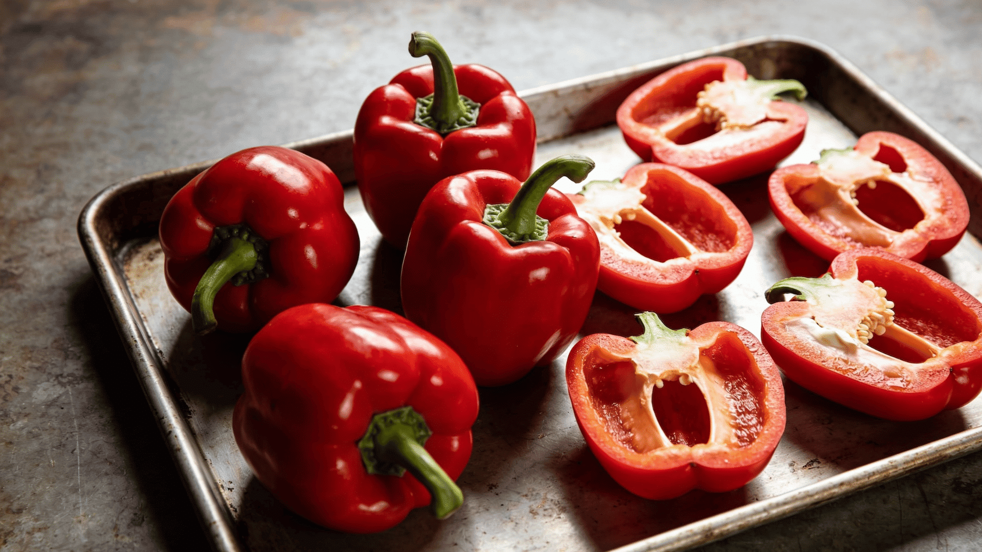 whole and halved red bell peppers arranged on a metal baking tray