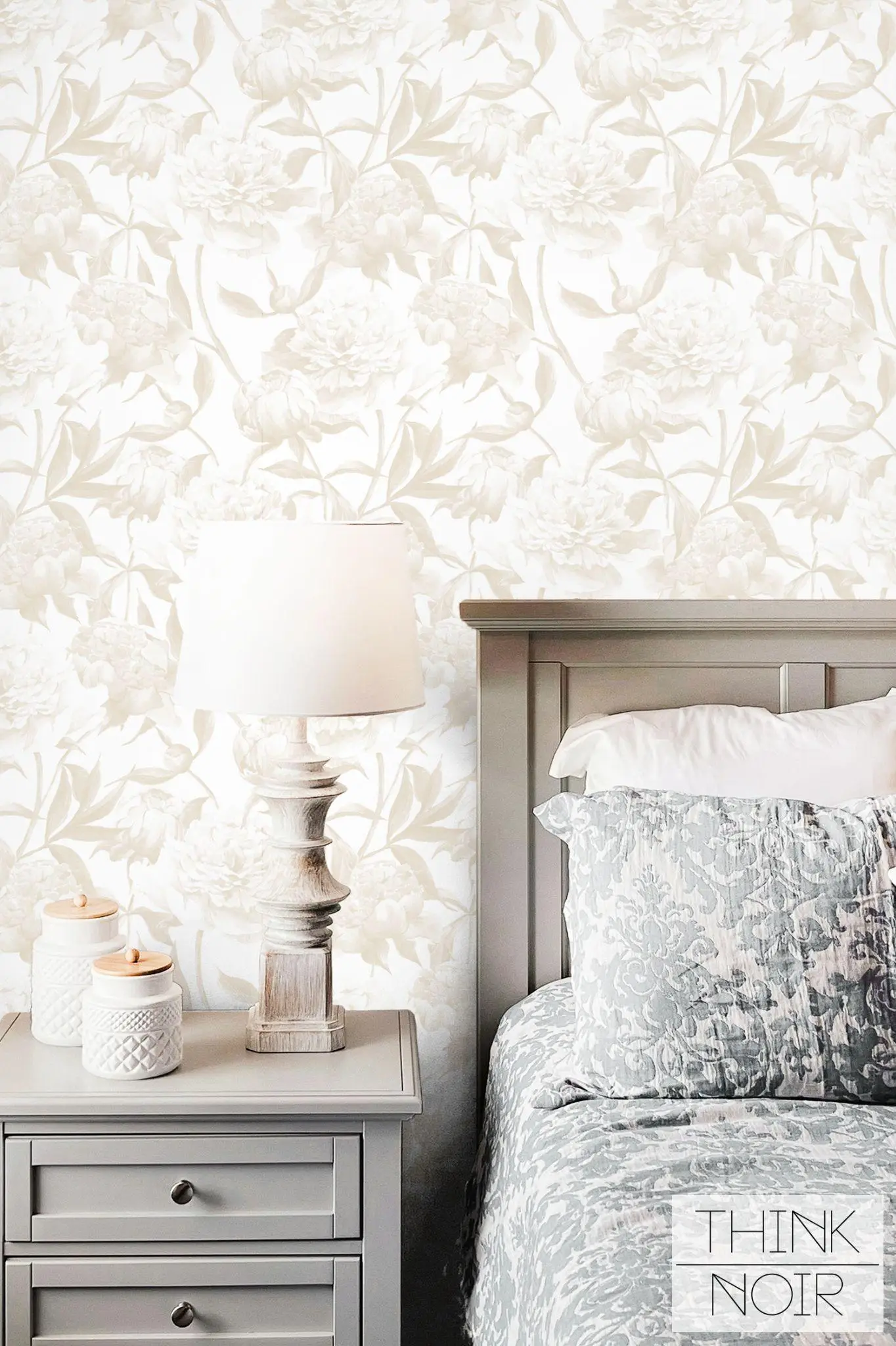 Pale floral wallpaper behind gray bedside table with lamp and patterned cushions