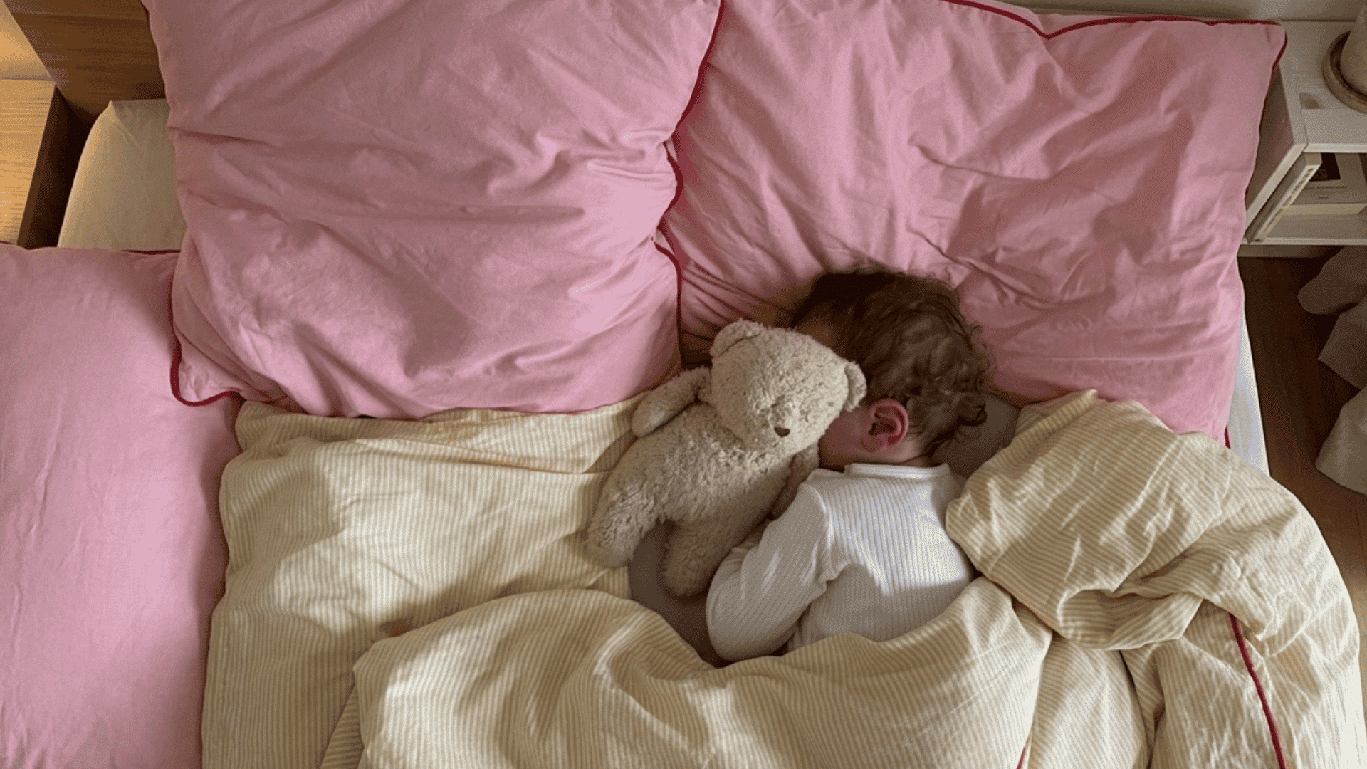 toddler sleeping with teddy bear under blanket on pink bedding