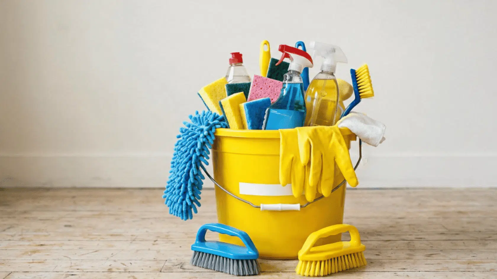 Yellow cleaning bucket with microfiber cloths, brushes, gloves, and household cleaning supplies for spring cleaning.