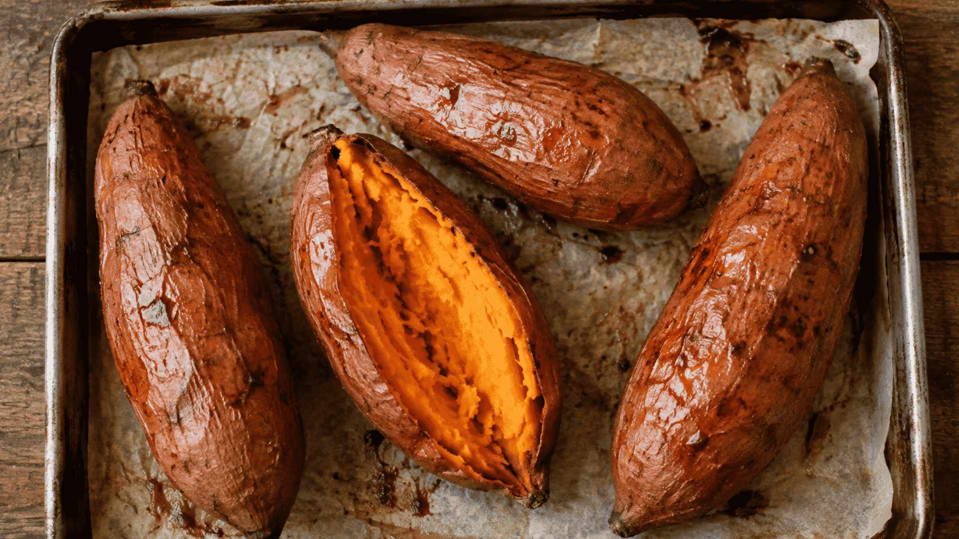 roasted sweet potatoes on a baking tray with one split open to show orange flesh