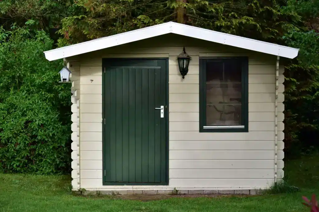 Small garden shed with green door and window surrounded by lush greenery