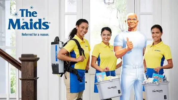 Three people in yellow uniforms with cleaning supplies indoors, with a cartoon character giving a thumbs-up