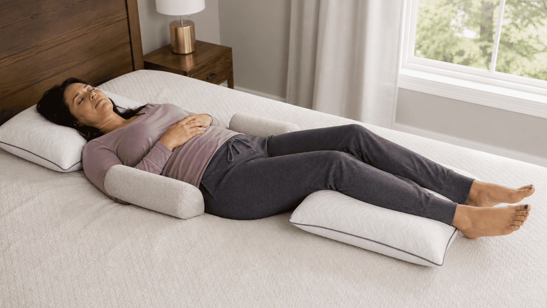 woman lying on her back in bed with pillows supporting her arms and legs for comfortable sleep.