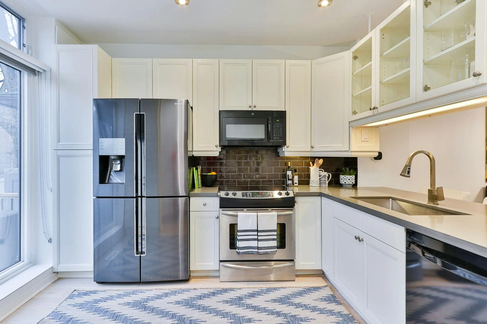 Modern kitchen with stainless steel appliances, white cabinets, and a blue patterned rug
