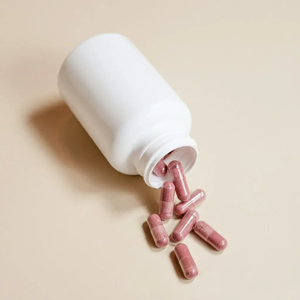 White bottle with pink capsules spilling on a beige surface
