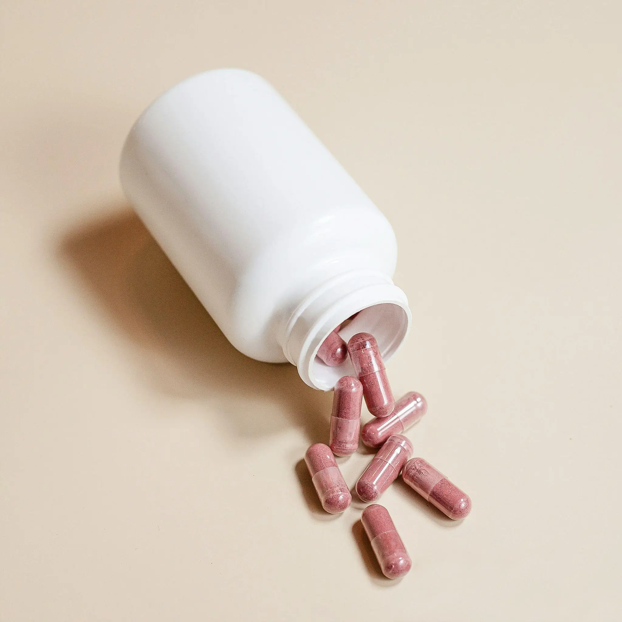 White bottle with pink capsules spilling on a beige surface