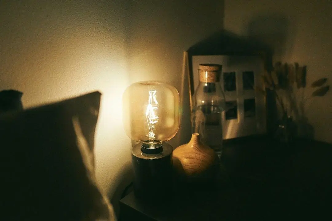 Vintage light bulb glowing on a dimly lit wooden desk with bottle and vase nearby