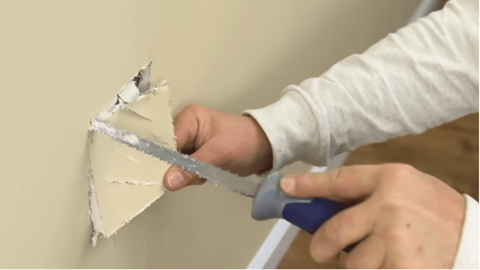 Cutting damaged drywall into a clean square for easier patching.