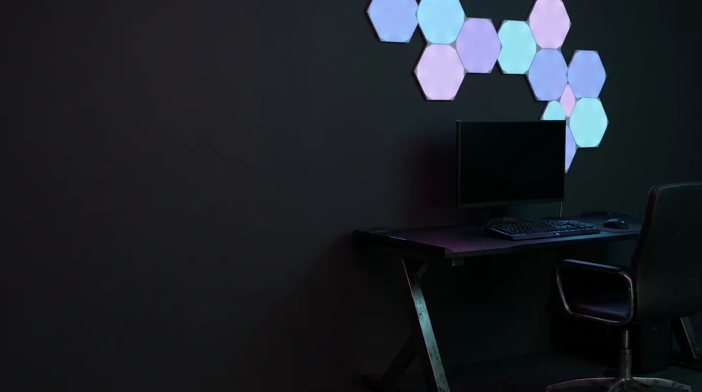 Computer desk with monitor and keyboard under hexagonal wall lights in dark room