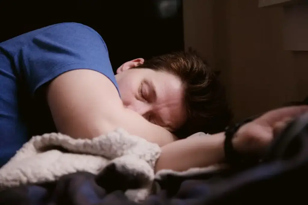 Person sleeping in a dimly lit room with blue shirt and cozy blanket