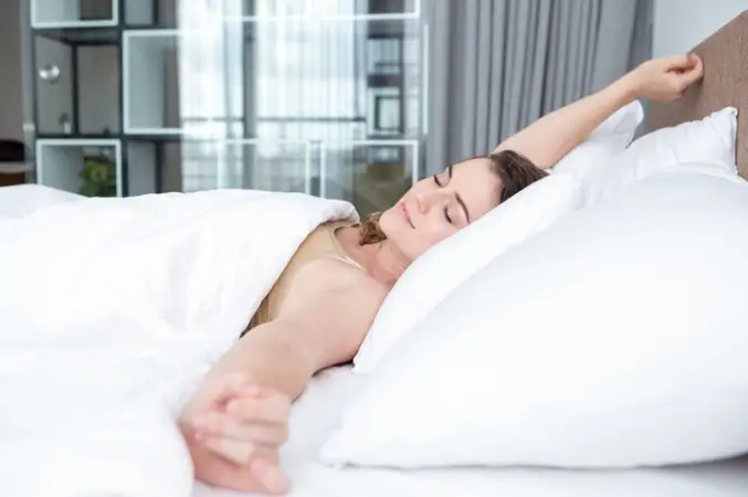 Person stretching in bed under white covers in a bright modern bedroom
