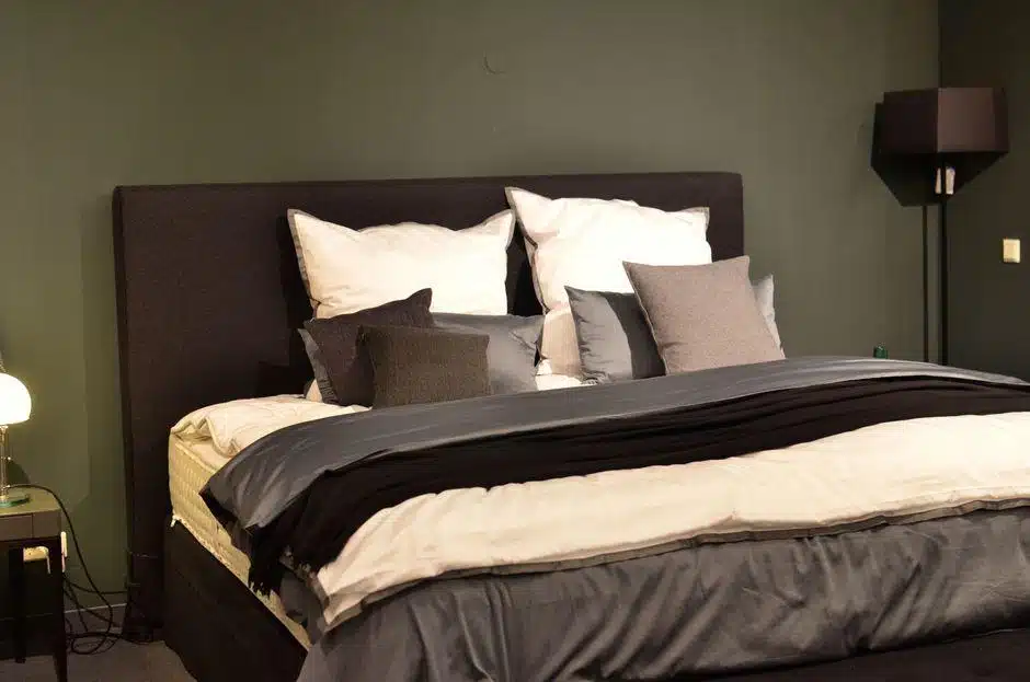 Black upholstered bed with white and gray pillows in a dimly lit bedroom