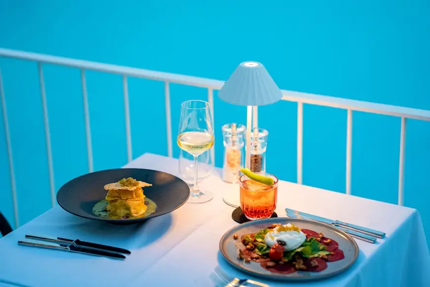 Elegant dinner setup with gourmet dishes and drinks on a patio table under warm lighting