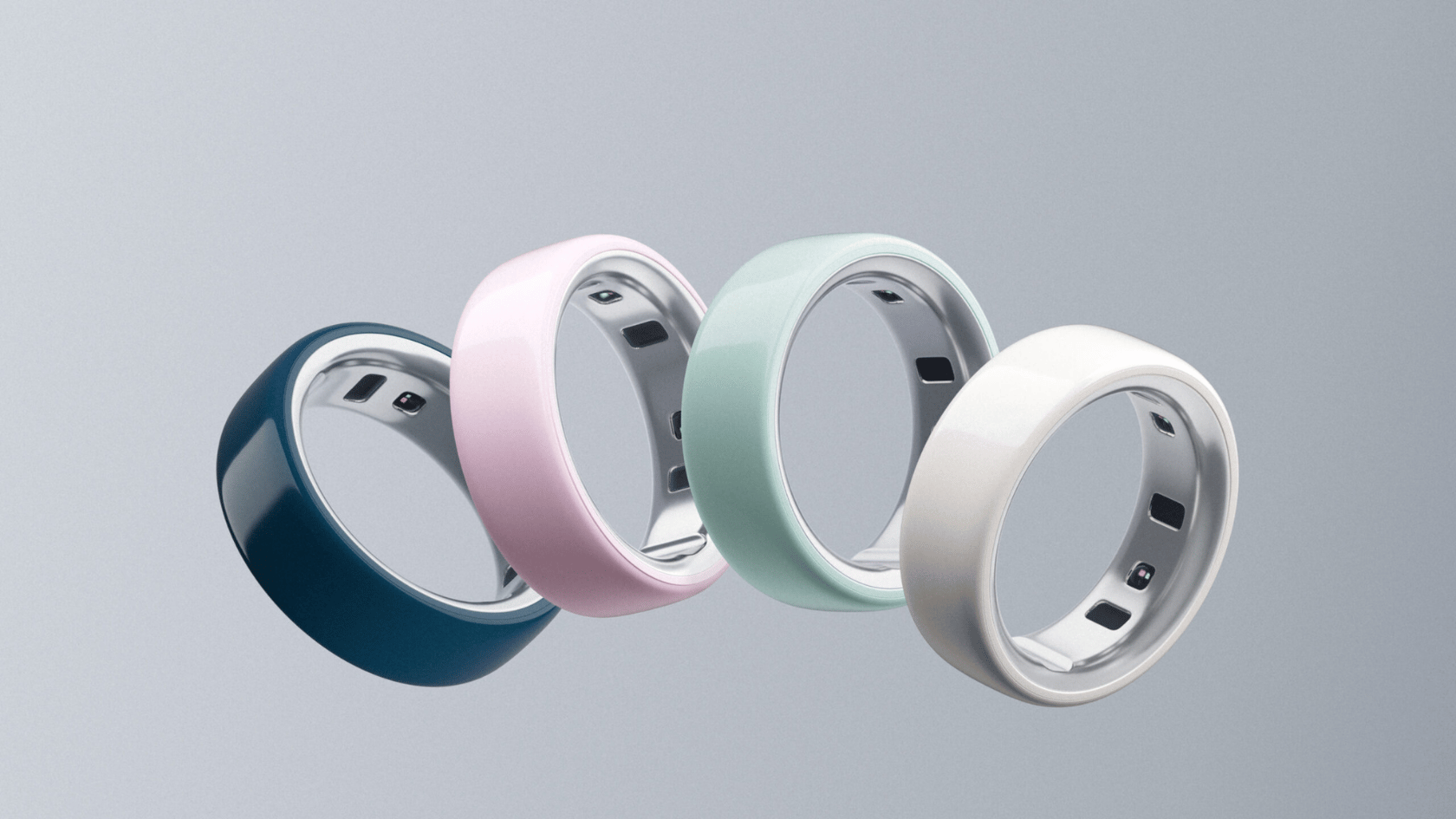 four oura rings in navy, pink, mint, and white arranged in an overlapping row against a gray background