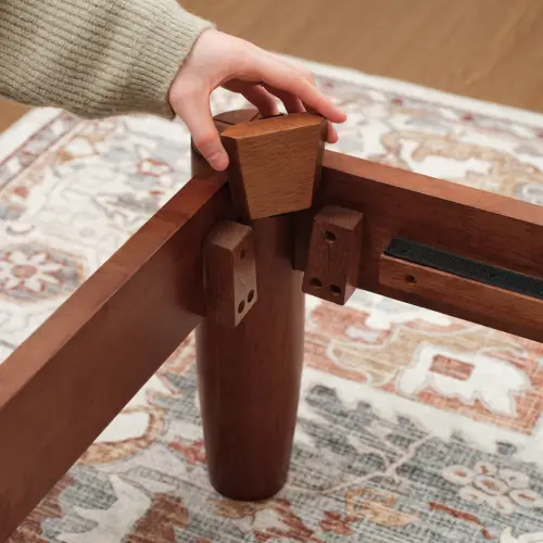 Hand assembling wooden furniture joint on patterned rug in bright room