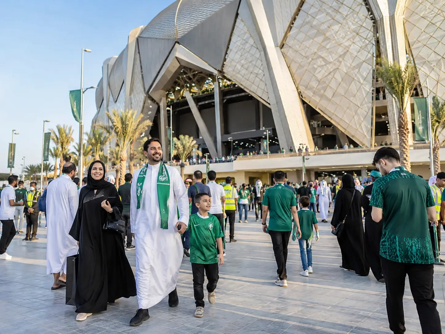 Crowd of people walking towards large modern stadium with geometric facade under clear sky