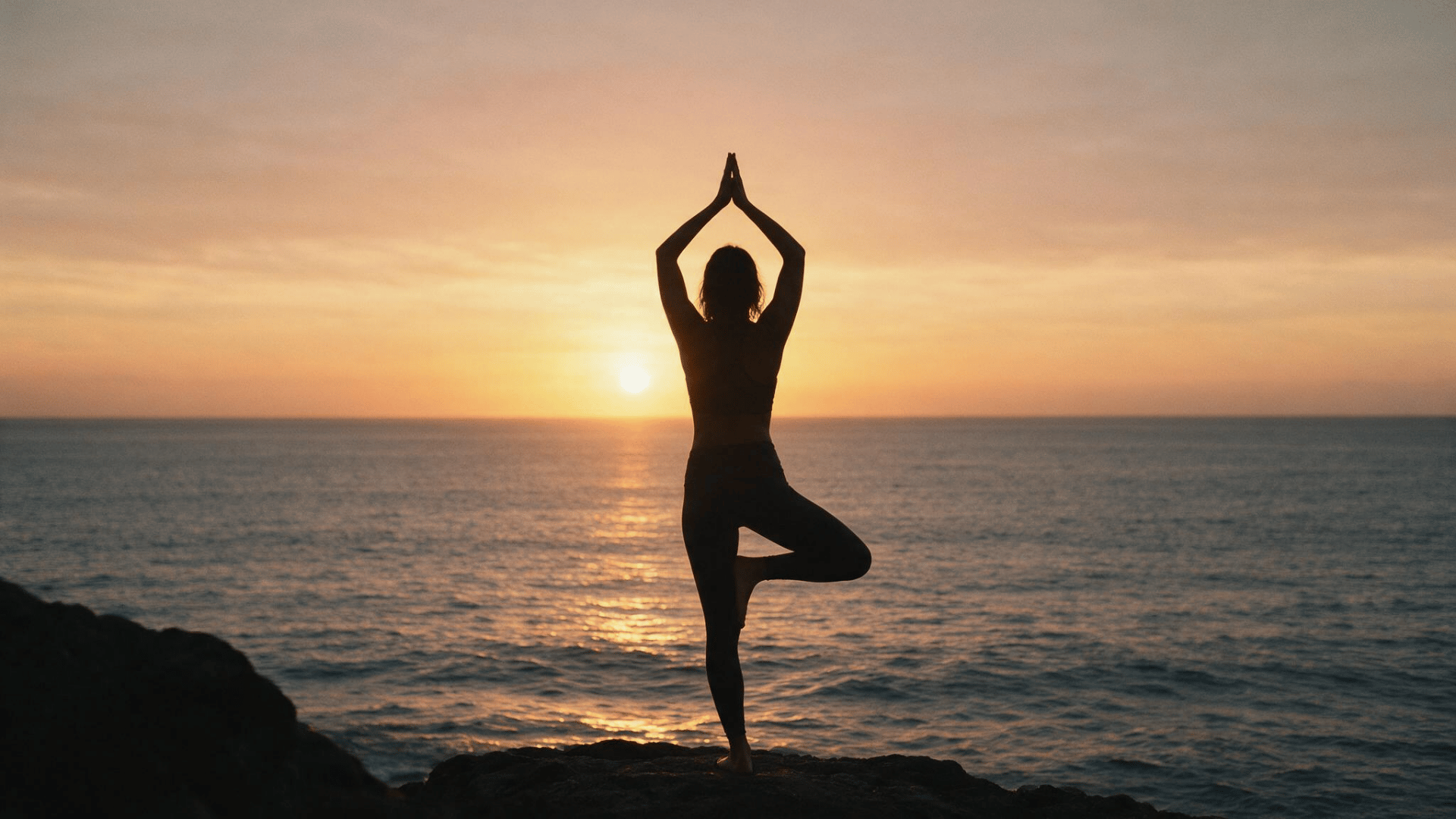 woman practicing yoga at sunrise by the ocean