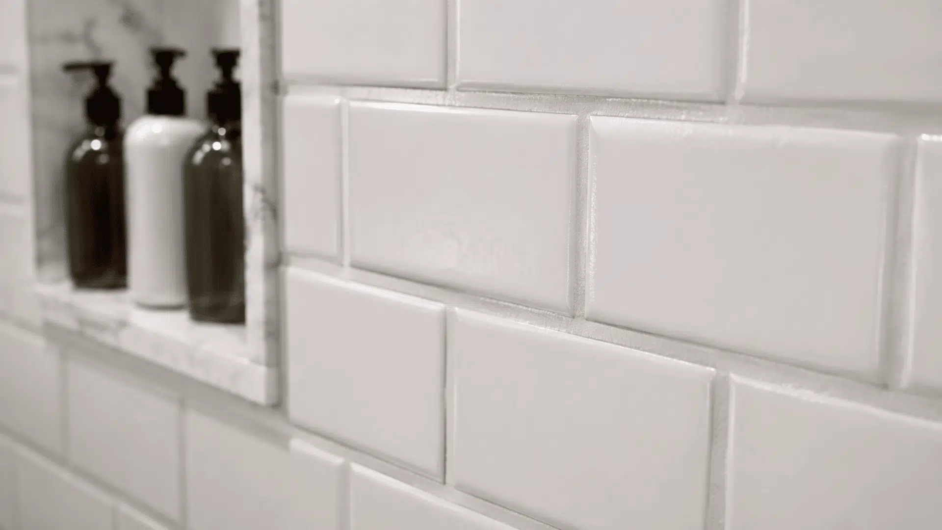 white subway bathroom tiles with smooth premixed grout lines beside a marble shelf and bottles
