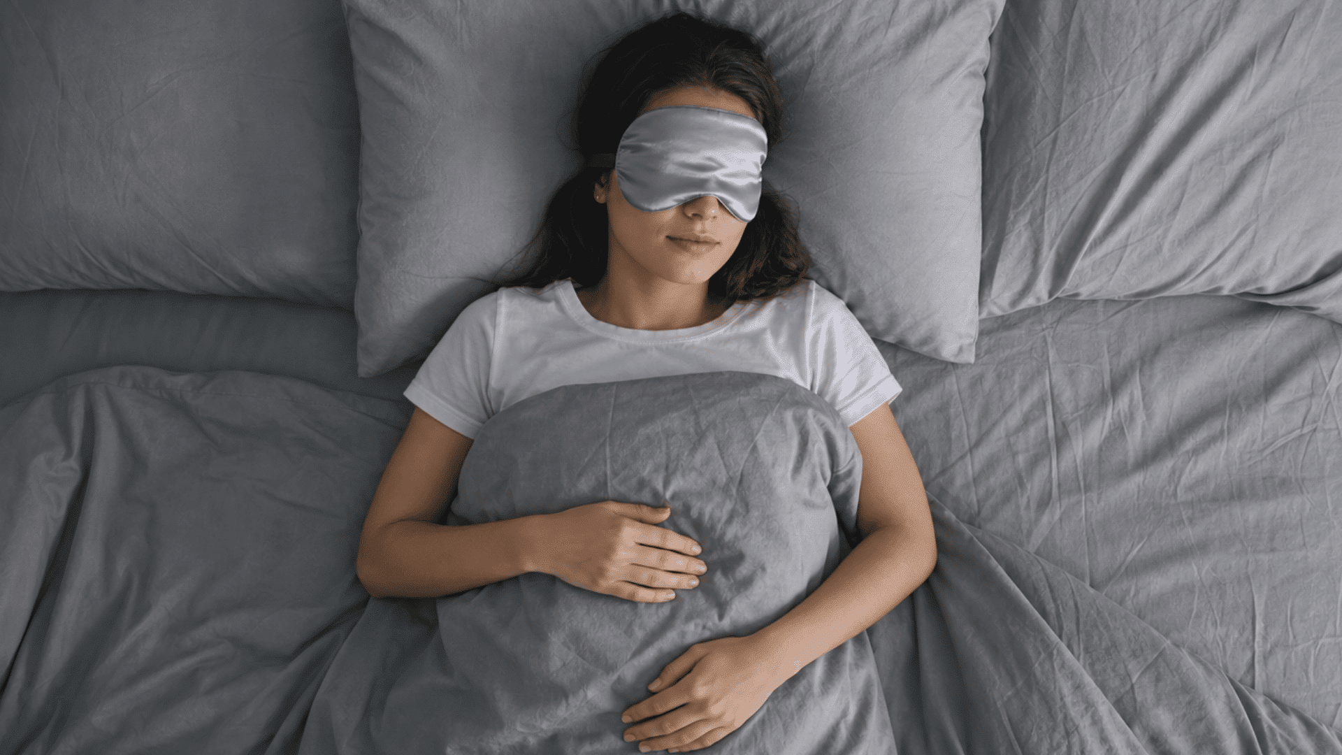 person sleeping peacefully in bed wearing an eye mask under a blanket at night.