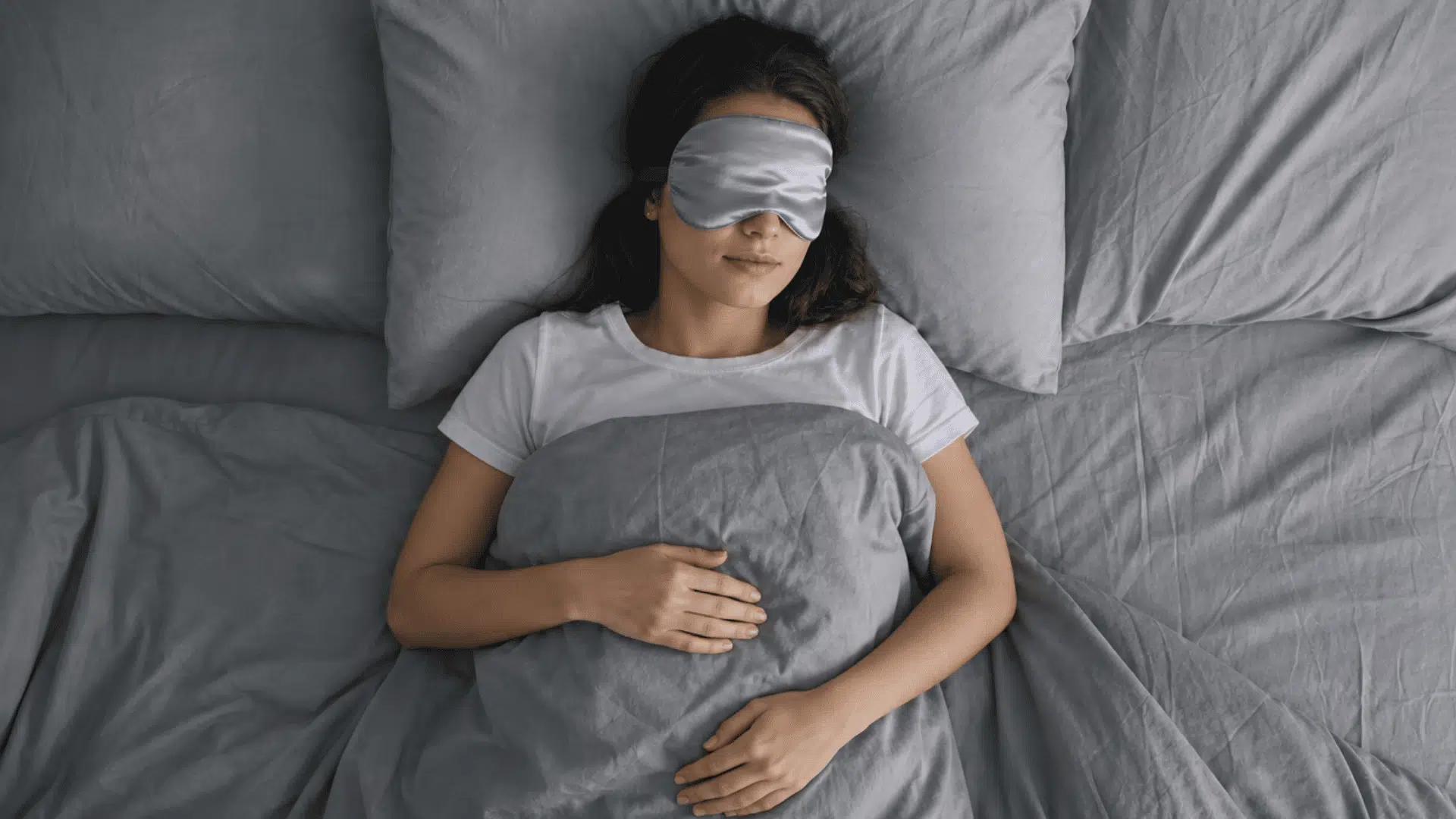 person sleeping peacefully in bed wearing an eye mask under a blanket at night.
