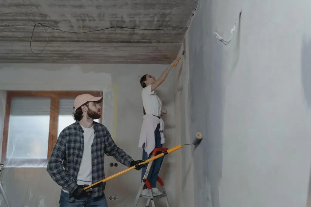 Two people painting a wall with rollers in a partially renovated room