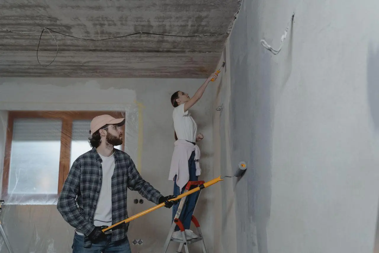 Two people painting a wall with rollers in a partially renovated room
