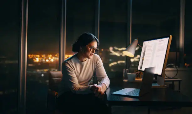 Person working at a computer in a dark office with city lights in background