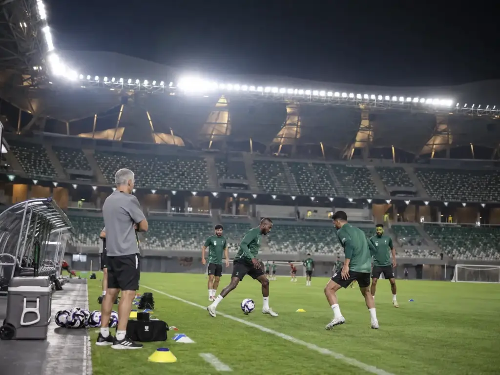 Football players in green jerseys training at night in a large stadium under bright lights