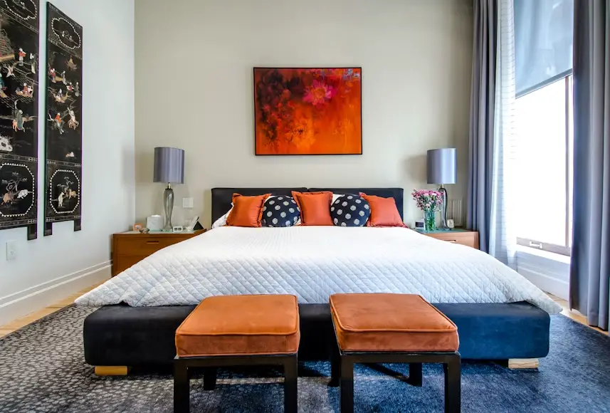 Bed with colorful pillows in modern bedroom with abstract artwork and side tables