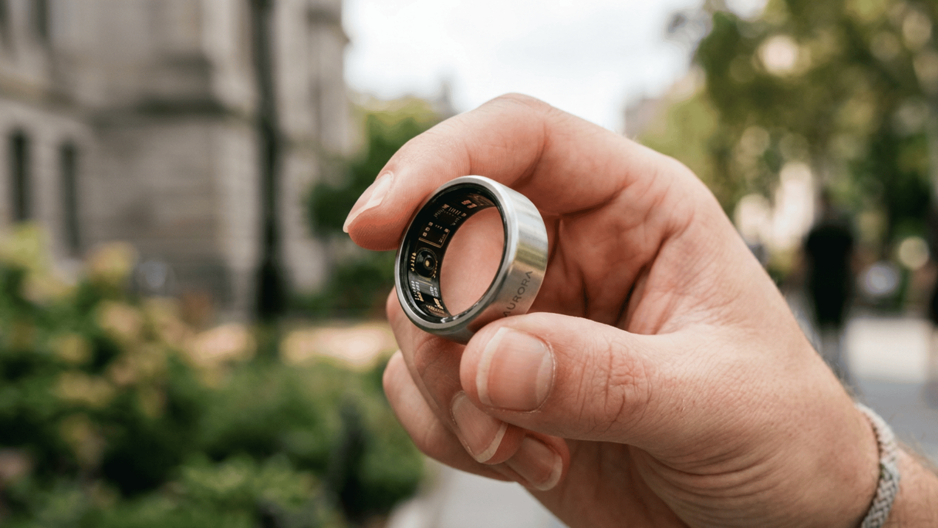 Hand holding silver Oura Ring outdoors showing its inner sensors used for sleep and health tracking.