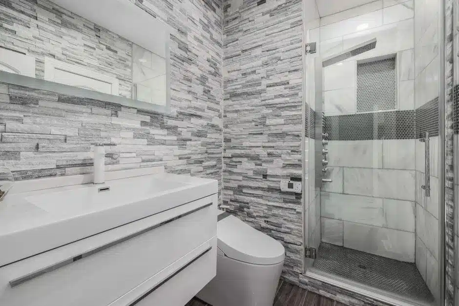 Modern bathroom with glass shower, large white sink, and gray textured stone walls