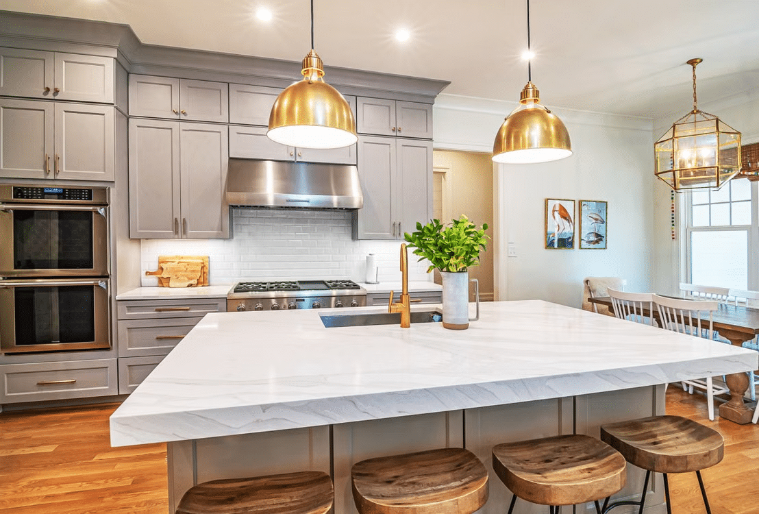 Modern kitchen with gray cabinets, marble island, brass pendant lights, and wooden stools