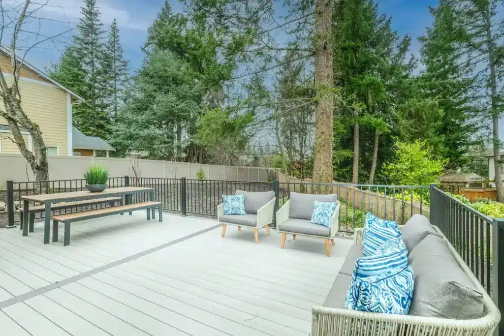 Spacious outdoor deck with grey seating and blue patterned cushions surrounded by lush green trees