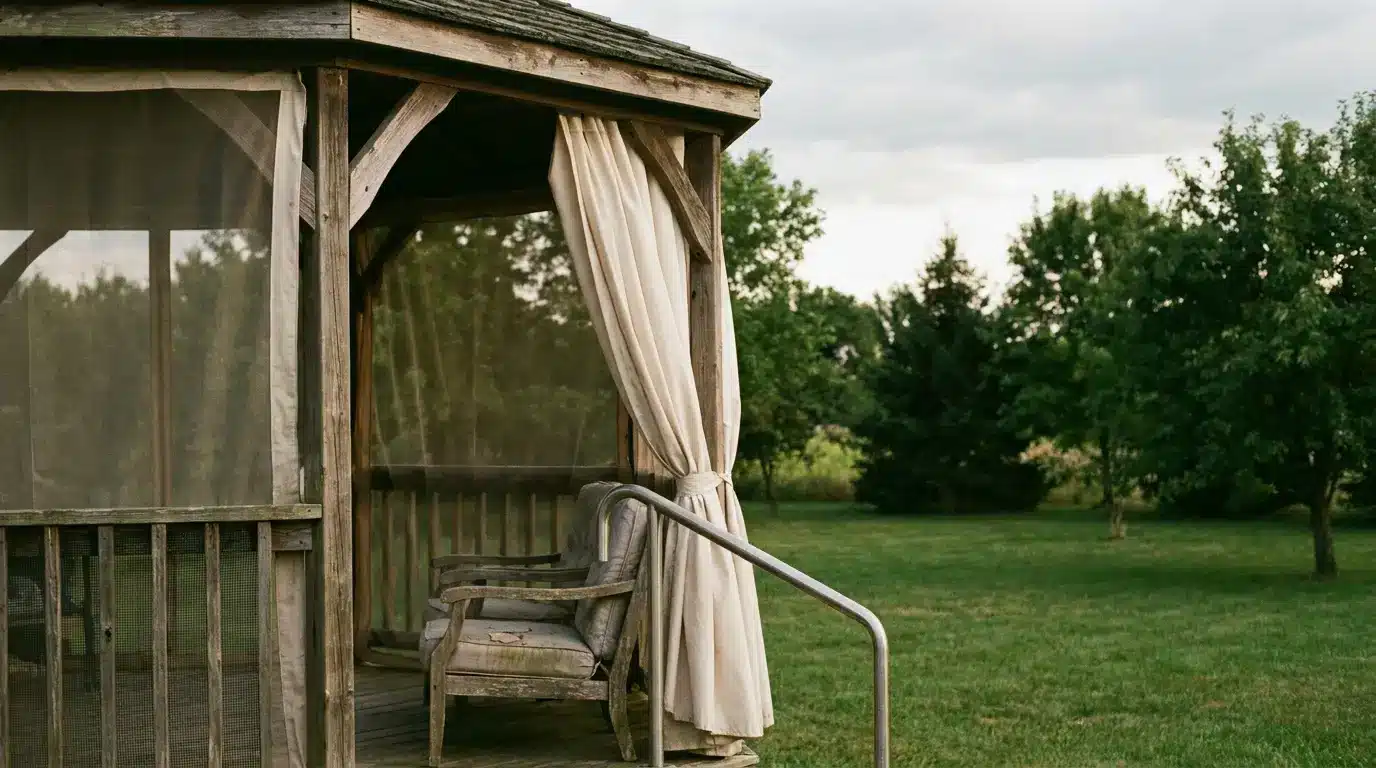 Wooden gazebo with draped curtains and armchair in a lush green garden setting