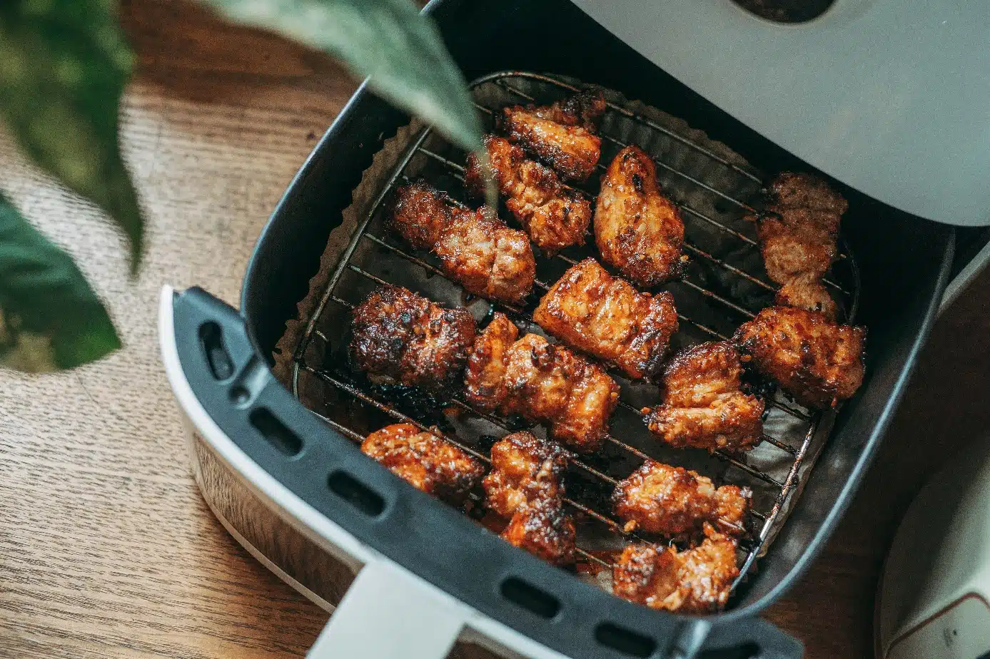 Crispy chicken wings in air fryer basket on wooden table