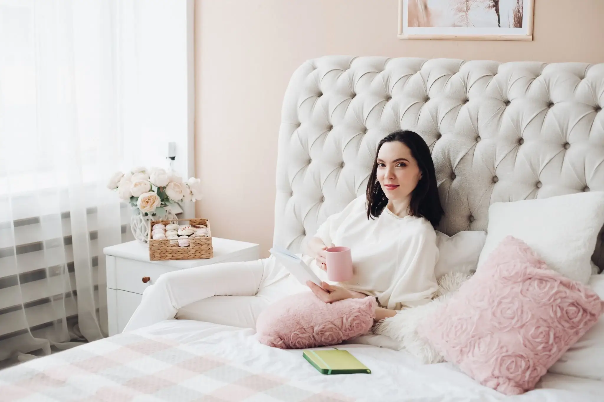Woman relaxing with tablet and coffee in bed with pink cushions